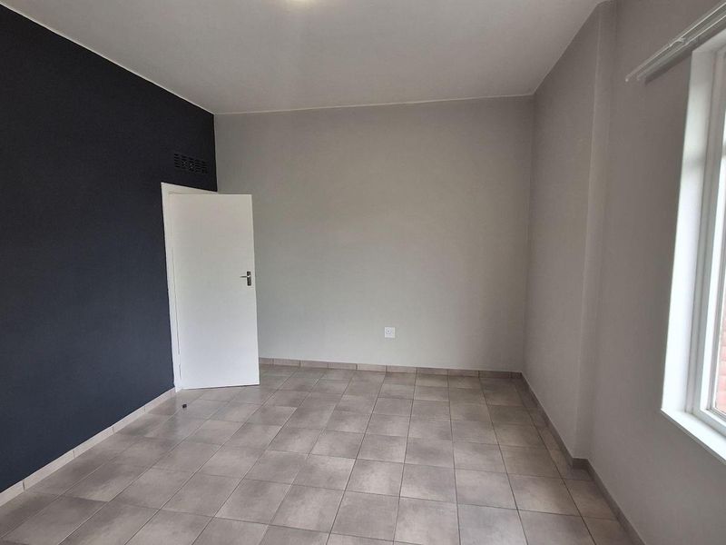 A bright, empty bedroom featuring neutral walls, a dark accent wall, and tiled flooring, offering a clean canvas for personalization.