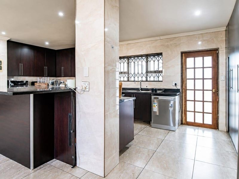Modern kitchen featuring dark wood cabinetry, granite countertops, tiled flooring, and a convenient layout with integrated appliances and direct exterior access.