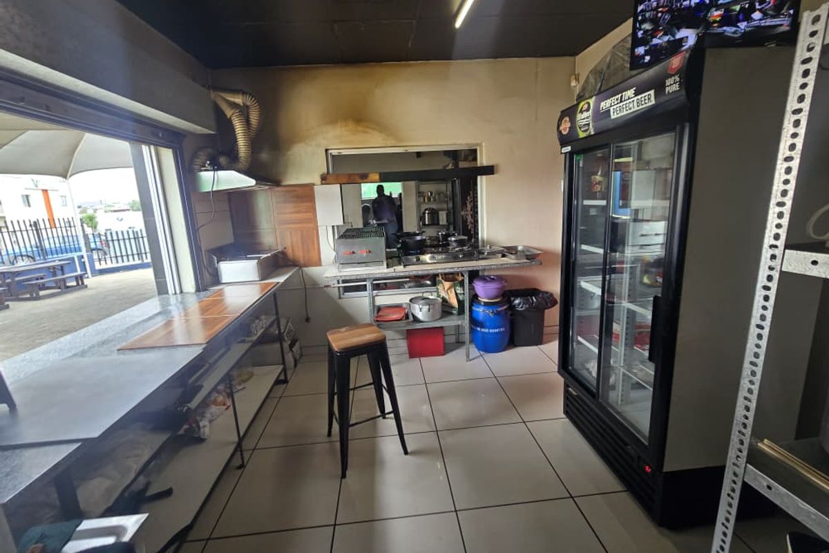 Commercial kitchen area featuring stainless steel prep counters, built-in cooking hobs, extractor fan, and tiled flooring with direct access to an outdoor patio.