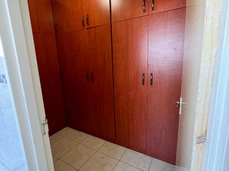 A bedroom featuring extensive built-in wooden cabinetry and tiled flooring, currently vacant and requiring minor finishing touches to the door frame.