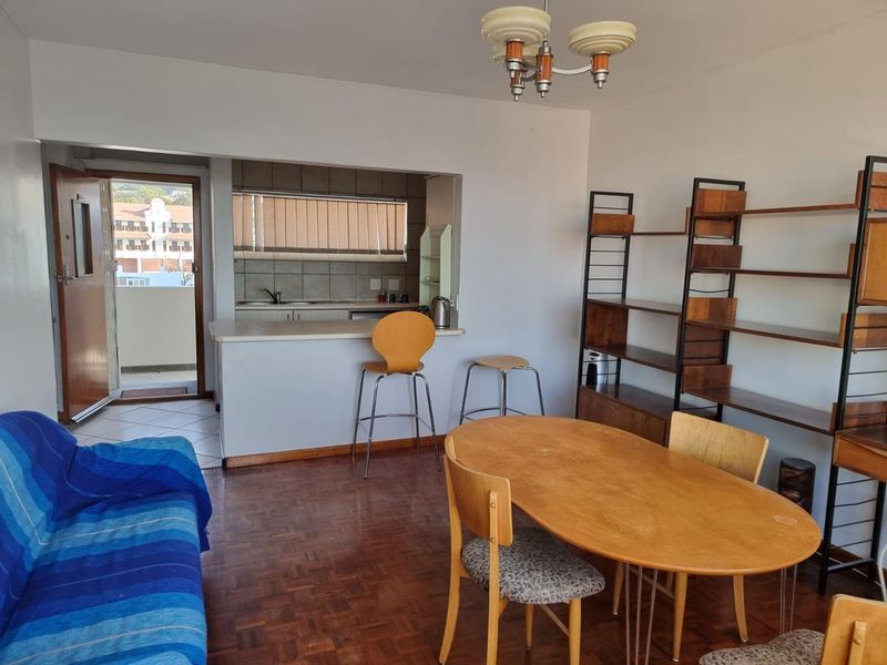 Open plan living and dining area featuring parquet flooring and a breakfast bar connecting to a functional kitchen space with tiled backsplash.