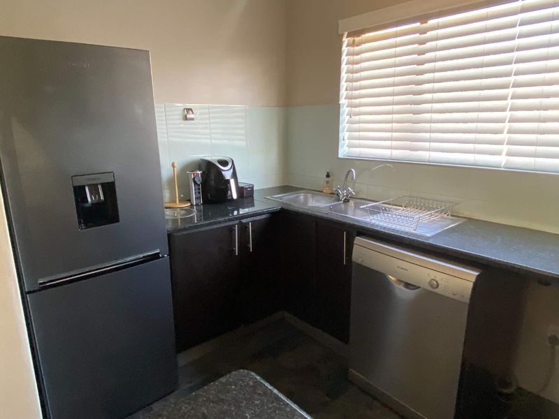 A functional kitchen featuring dark wood cabinetry, laminate countertops, a stainless steel sink, and a tiled splashback with natural light from a window.