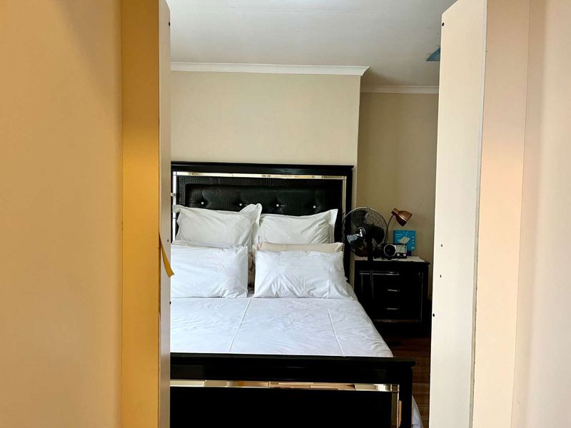 A bedroom view through a doorway, featuring neutral wall tones and visible ceiling damage requiring repair.