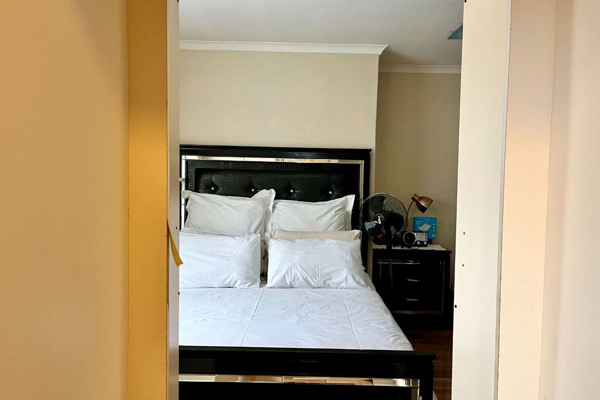 A bedroom view through a doorway, featuring neutral wall tones and visible ceiling damage requiring repair.