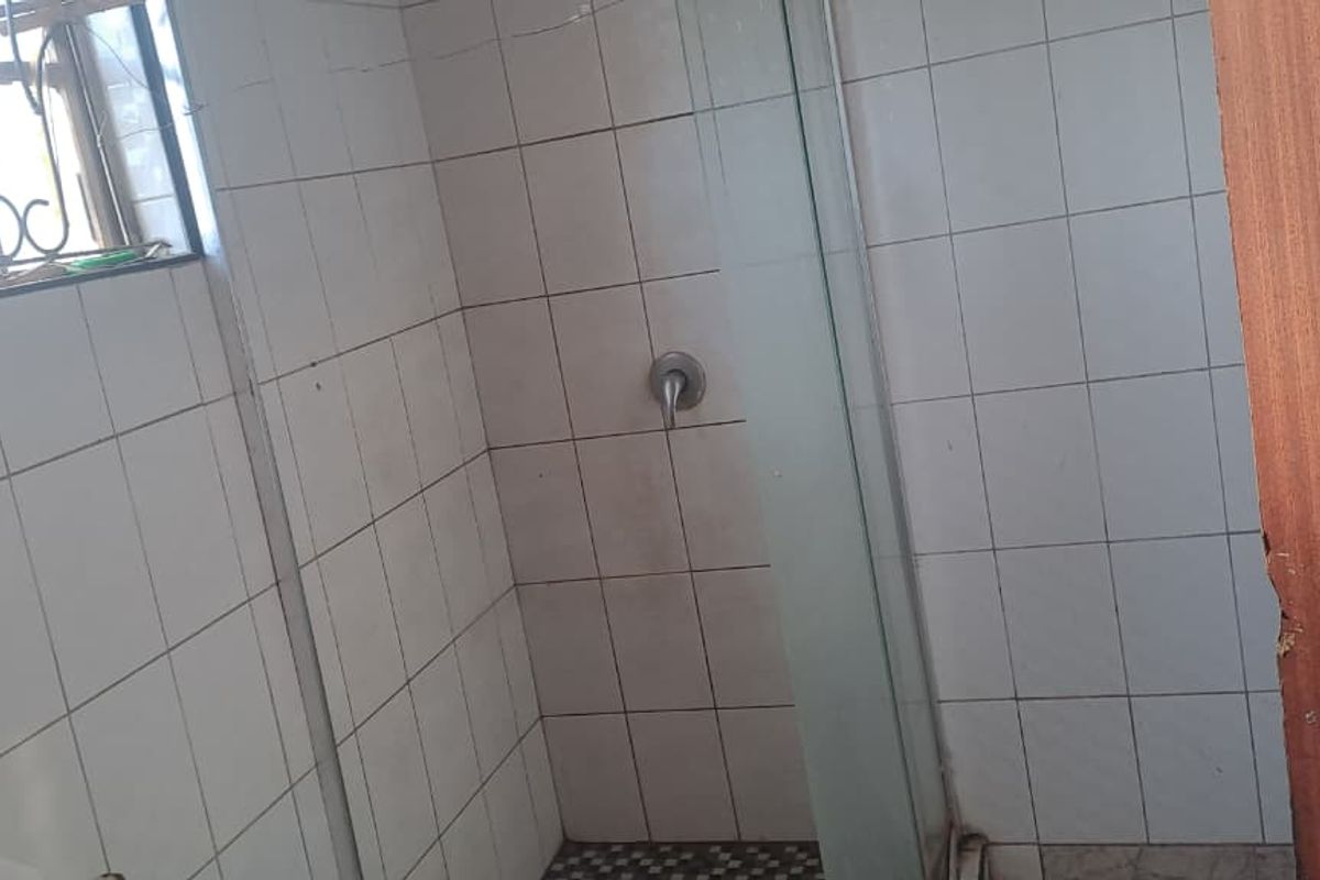 A functional bathroom featuring a tiled shower enclosure with a glass door and a window with security bars.