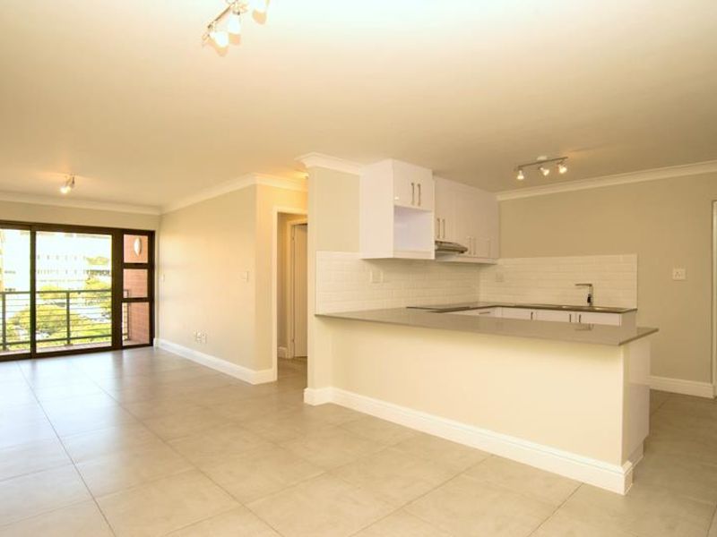 Modern open-plan apartment featuring a sleek kitchen with stone countertops, subway tile backsplash, and seamless flow to a bright living area with balcony access.