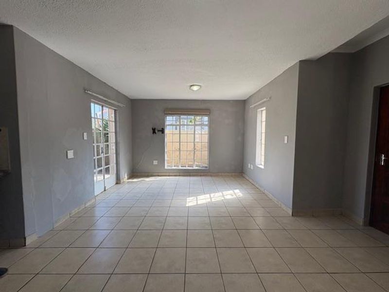 A spacious, empty living area featuring neutral tiled flooring, large windows, and access to the exterior via french doors.