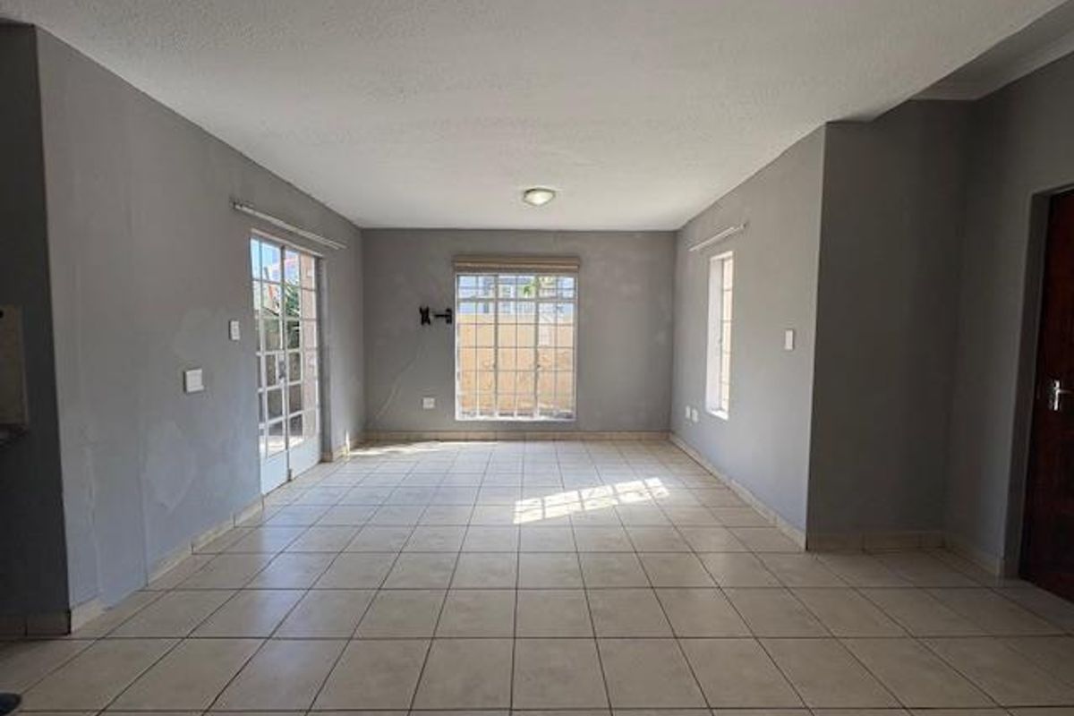 A spacious, empty living area featuring neutral tiled flooring, large windows, and access to the exterior via french doors.