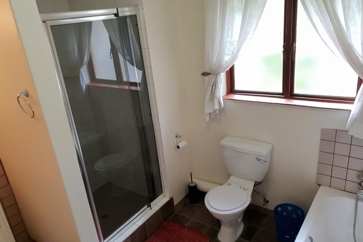 A functional bathroom featuring a glass-enclosed shower, a standard toilet, and a bathtub with tiled surrounds and natural light from the window.