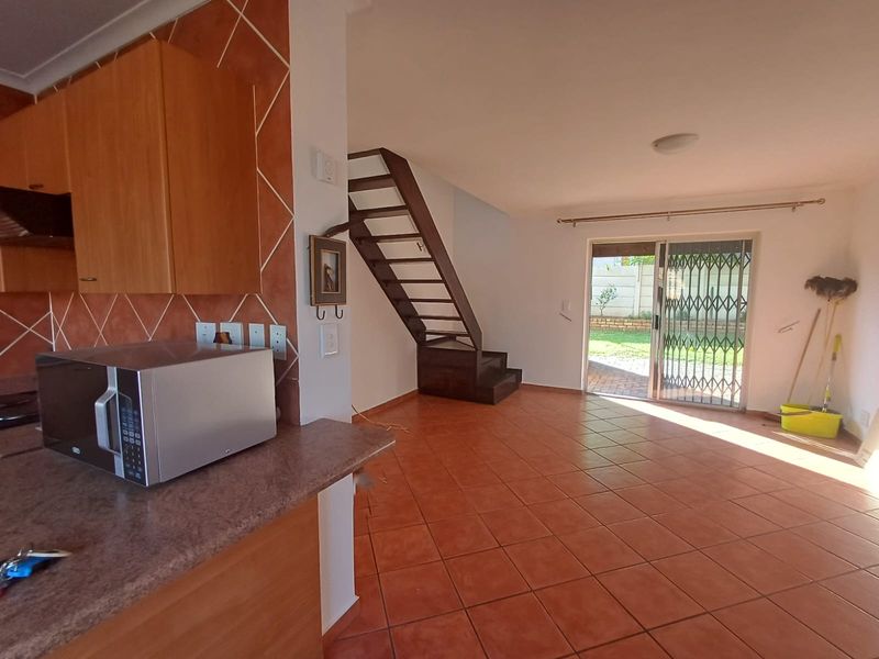 Open-plan living area featuring tiled flooring, a functional kitchen with cabinetry, and direct access to the rear garden through a sliding glass door.