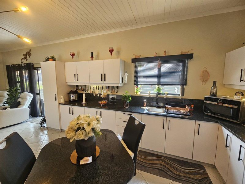 A functional kitchen featuring white cabinetry, dark granite countertops, a stainless steel sink, and tiled flooring, with direct access to the adjacent living area.
