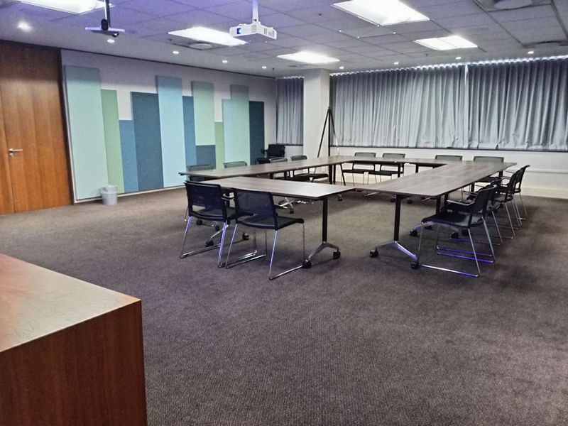 A professional office meeting room featuring acoustic wall paneling, a suspended ceiling with recessed lighting, and integrated projector equipment.