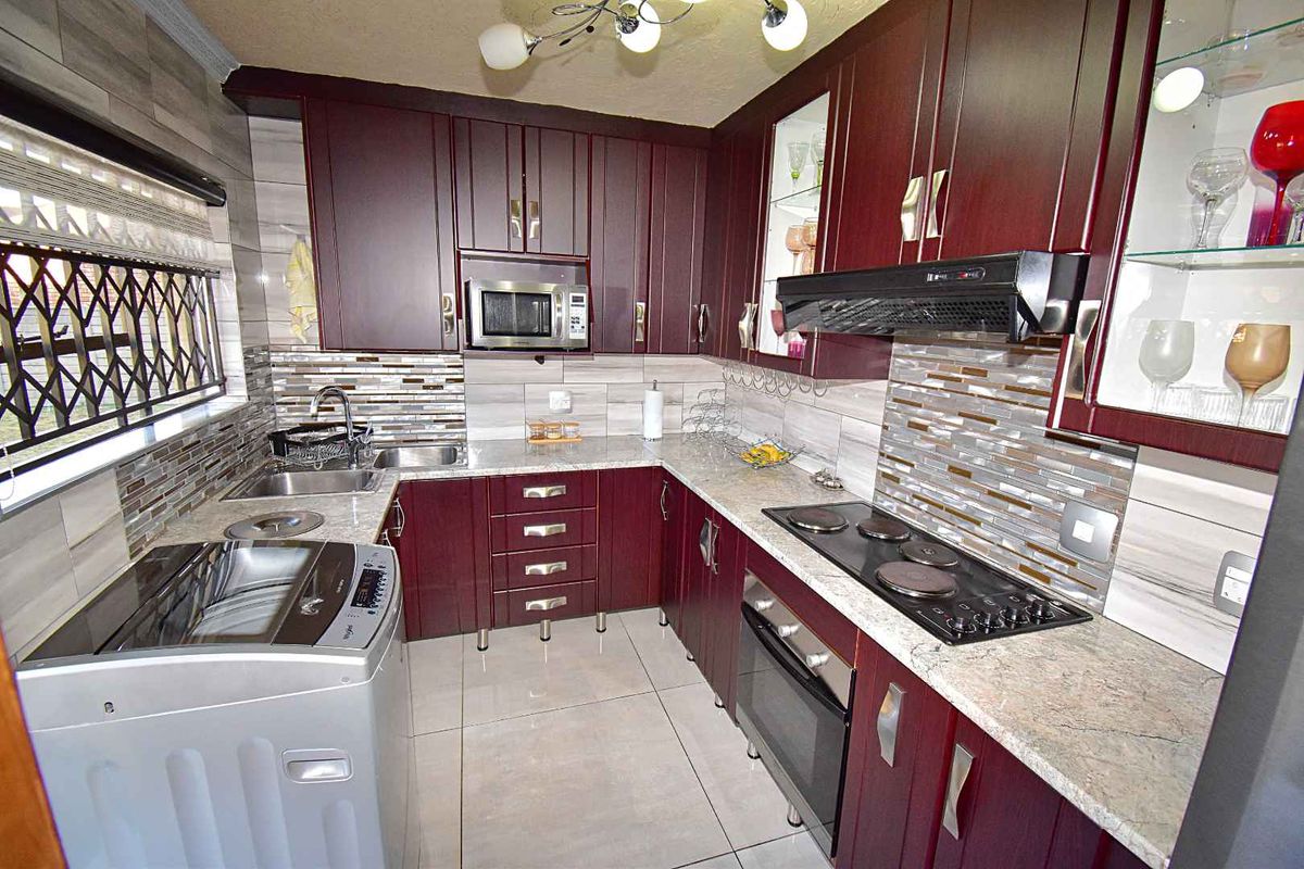 A well-maintained kitchen featuring dark wood cabinetry, granite countertops, a built-in oven, electric hob, extractor fan, and a tiled backsplash.