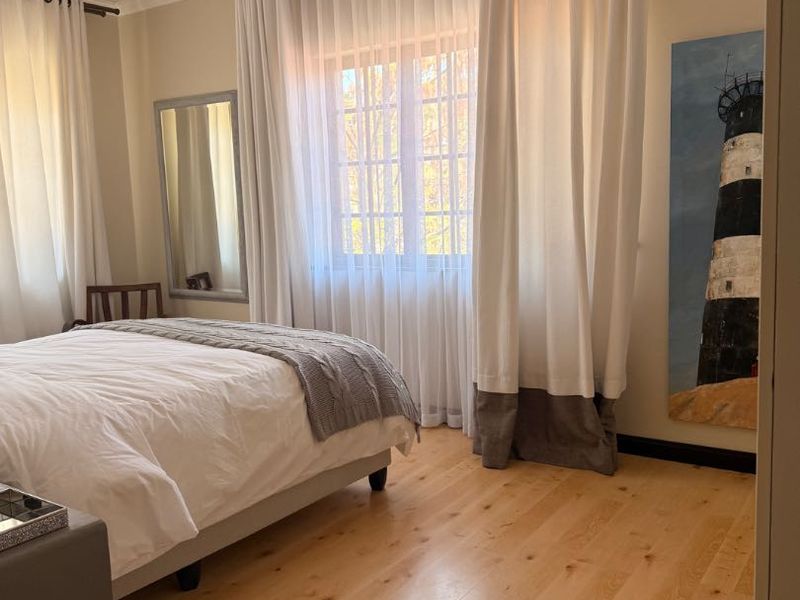 A bright and well-maintained bedroom featuring light timber flooring, a ceiling fan, and large windows dressed with elegant floor-to-ceiling curtains.