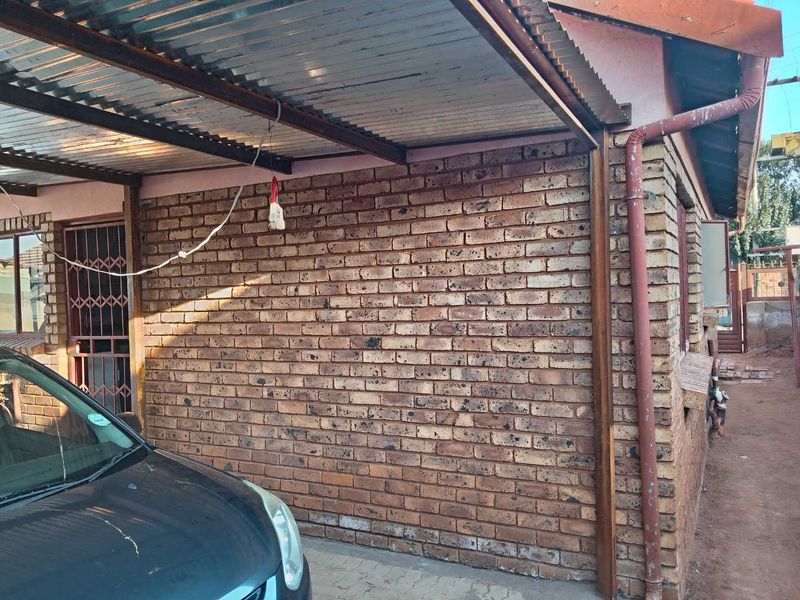 Exterior view of a brick-faced property featuring a corrugated metal carport structure and security gate access.