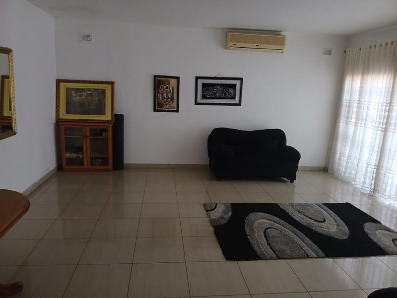 A spacious living area featuring neutral tiled flooring and a wall-mounted air conditioning unit, offering a clean and functional layout.
