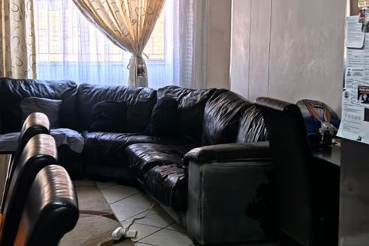 A living room area featuring tiled flooring and an arched doorway, currently showing signs of wear on the wall surfaces.
