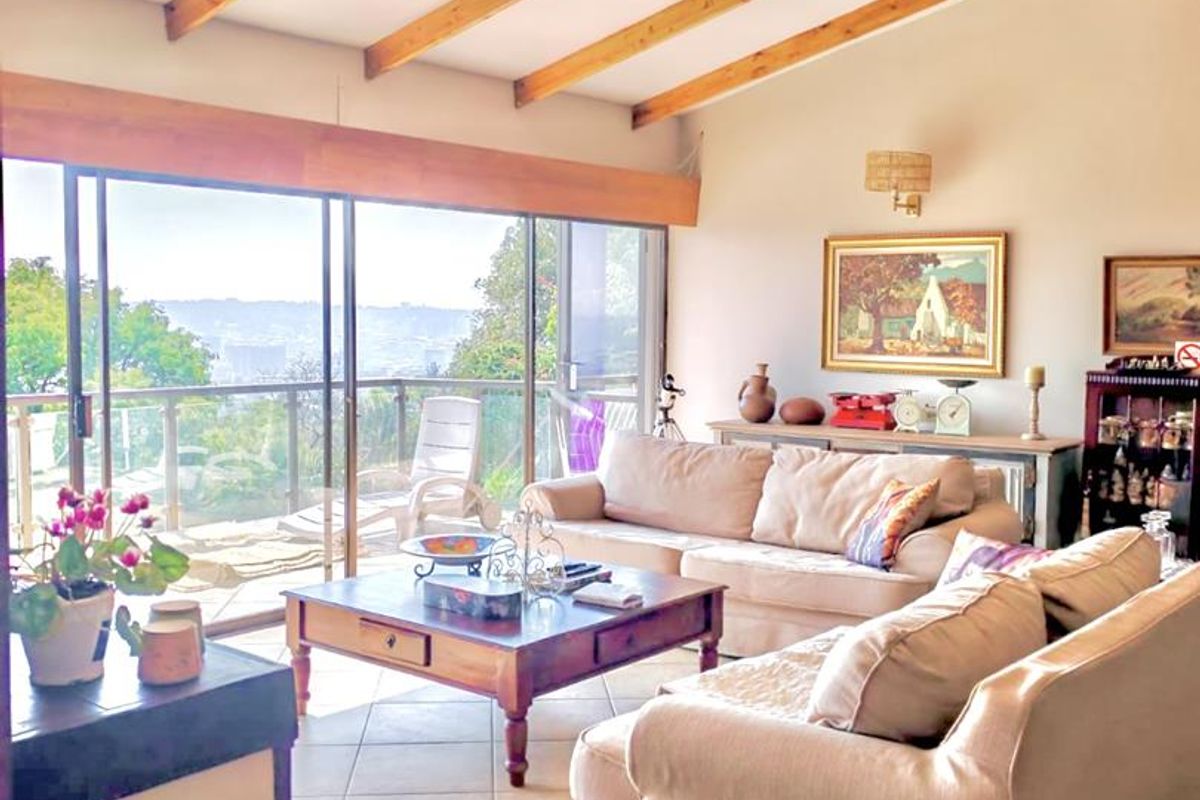 A bright living room featuring exposed timber ceiling beams, tiled flooring, and large sliding glass doors that open onto a balcony with scenic views.