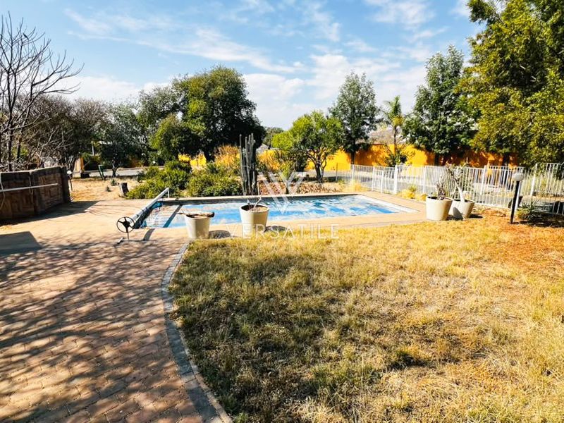 Outdoor pool area featuring a paved walkway, swimming pool with cover, and surrounding garden space with perimeter fencing.