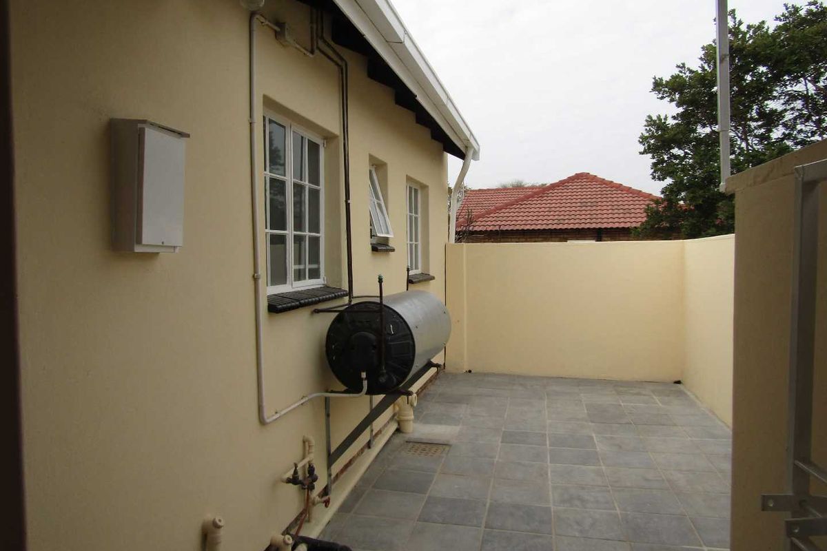 A paved rear courtyard area featuring an exterior wall-mounted water heater, drainage points, and perimeter boundary walls.