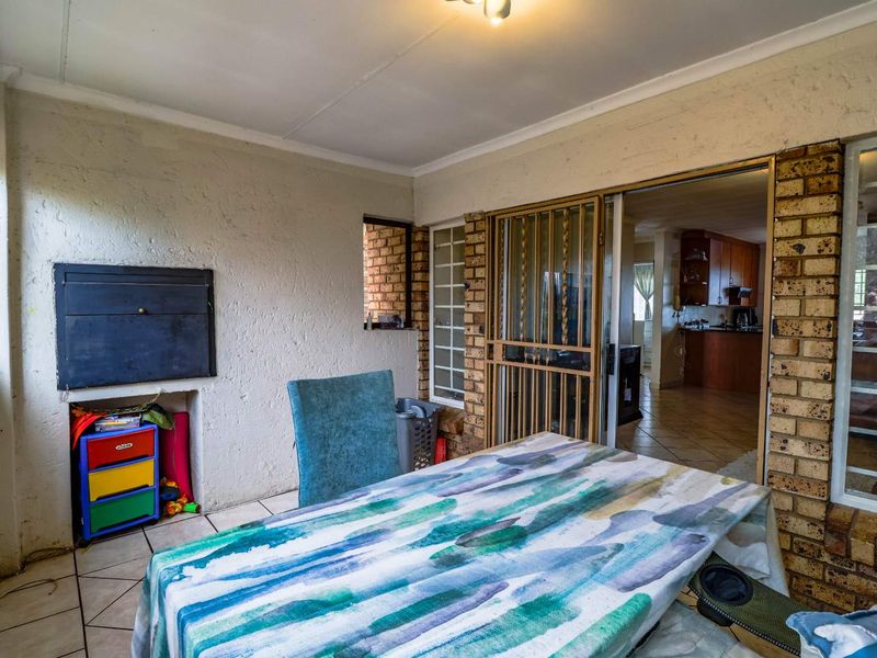 Covered patio area featuring a built-in braai, brick accent wall, and tiled flooring, providing direct access to the interior living space.