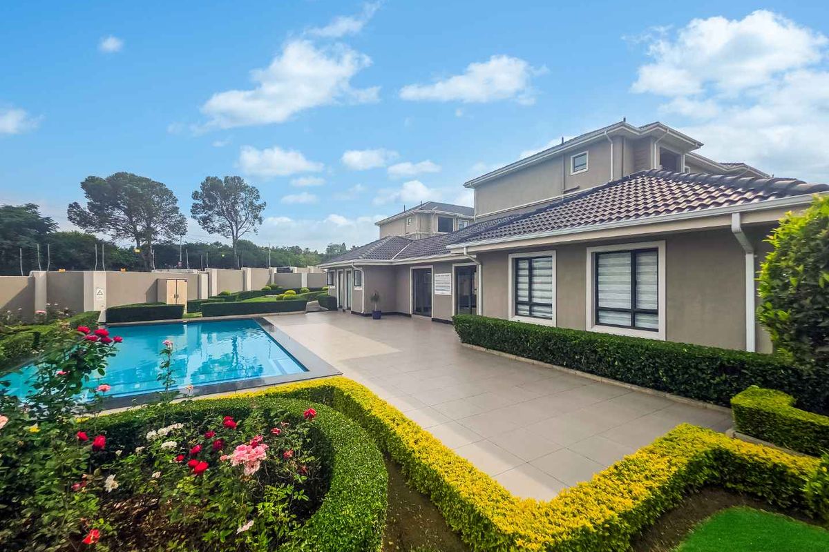 A well-maintained rear exterior view featuring a swimming pool, paved patio area, and landscaped garden beds surrounding the property.