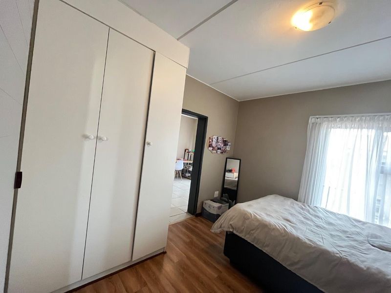 A bedroom featuring laminate flooring and built-in cupboards, with a view through the doorway into an adjacent living space.