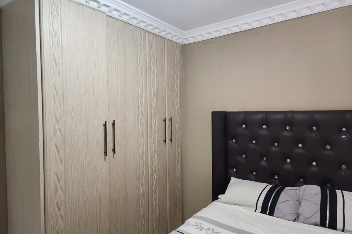 A well-maintained bedroom featuring light wood-grain built-in wardrobes and decorative ceiling cornicing.