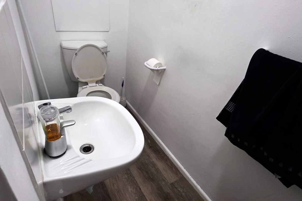 A compact office bathroom featuring a white toilet, a wall-mounted washbasin with a modern faucet, and durable laminate flooring.