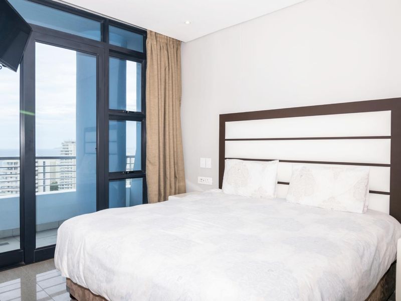 A well-maintained bedroom featuring large aluminium sliding doors that provide natural light and access to a balcony with coastal views.