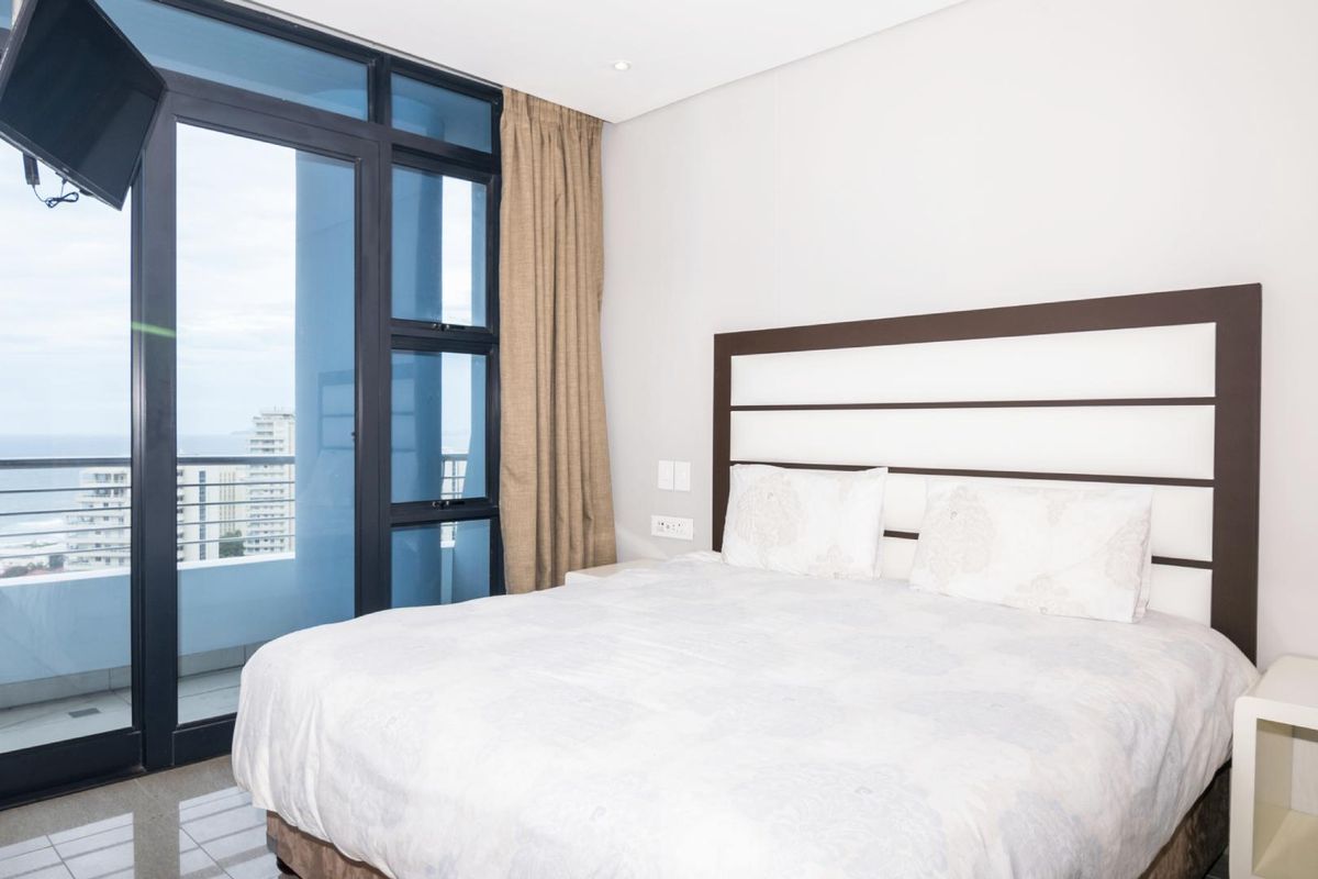 A well-maintained bedroom featuring large aluminium sliding doors that provide natural light and access to a balcony with coastal views.