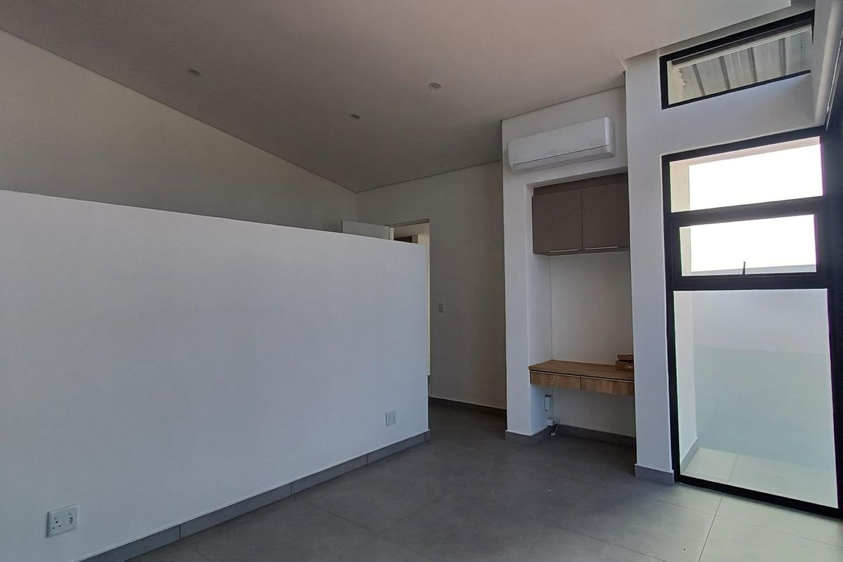 Modern bedroom featuring tiled flooring, a built-in desk with overhead storage, split-system air conditioning, and large windows providing natural light.