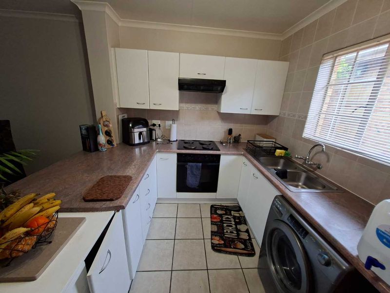 A functional U-shaped kitchen featuring white cabinetry, laminate countertops, a built-in oven with hob, and tiled flooring with a dedicated space for a washing machine.