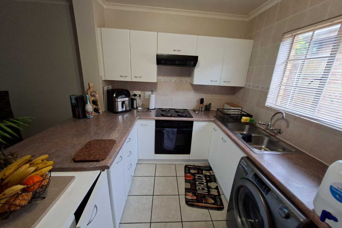 A functional U-shaped kitchen featuring white cabinetry, laminate countertops, a built-in oven with hob, and tiled flooring with a dedicated space for a washing machine.