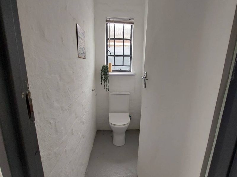 A compact, minimalist guest toilet featuring painted brick walls, a steel-framed window, and a standard toilet suite.