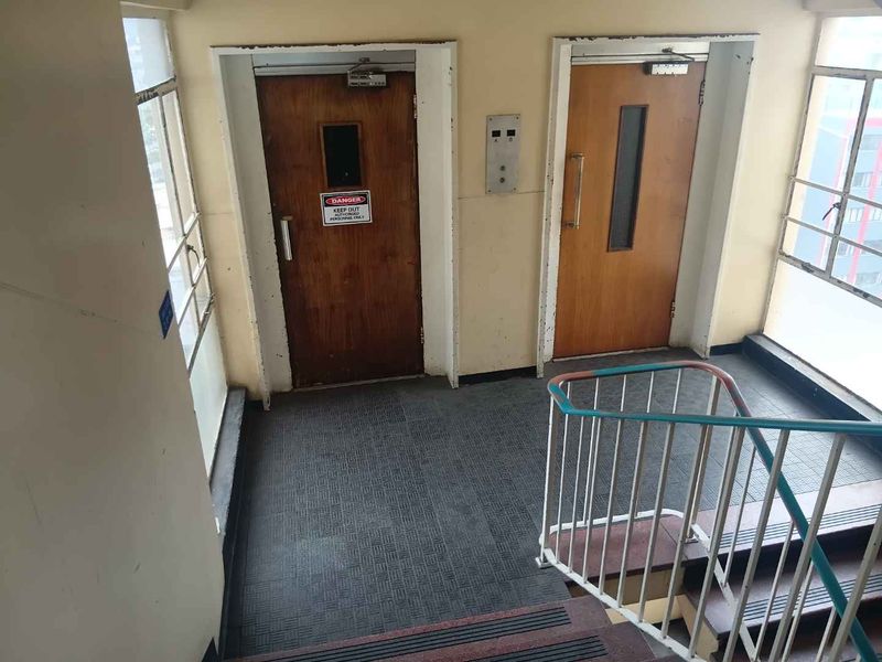 A functional apartment building hallway featuring elevator access, a staircase with metal railings, and tiled flooring in a dated condition.