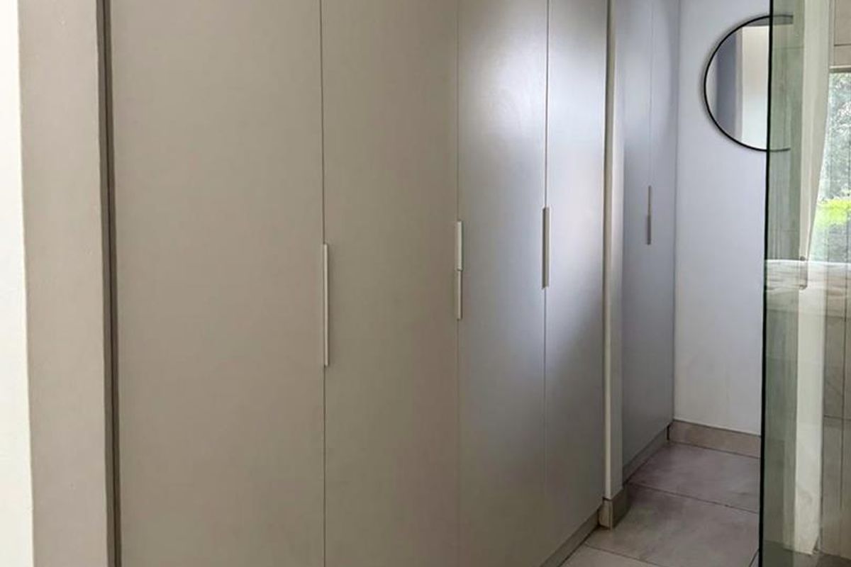 A modern bedroom area featuring floor-to-ceiling built-in cupboards, neutral tiled flooring, and an adjacent glass-enclosed shower.