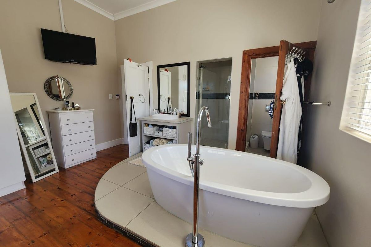 Spacious bathroom featuring a freestanding bathtub on a tiled plinth, separate shower, vanity, and timber flooring.