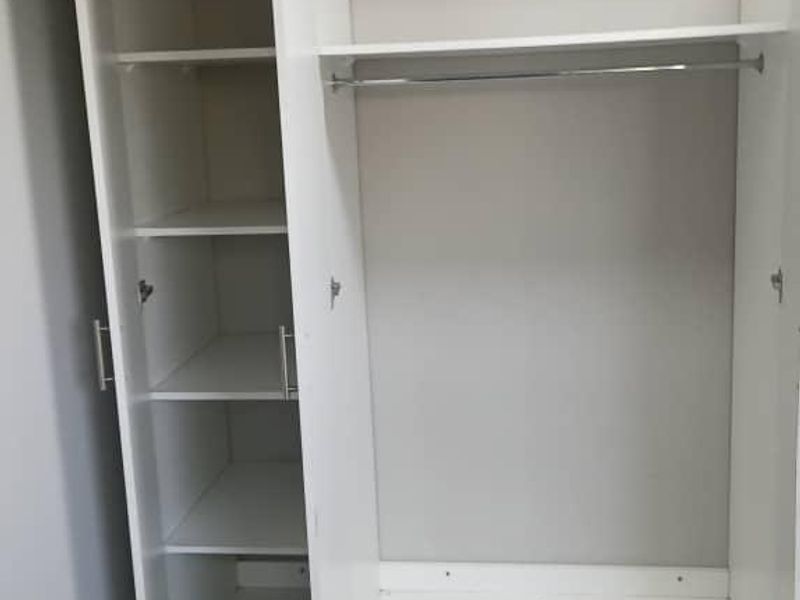 A functional built-in wardrobe with shelving and hanging space, featuring clean white finishes and durable tiled flooring.