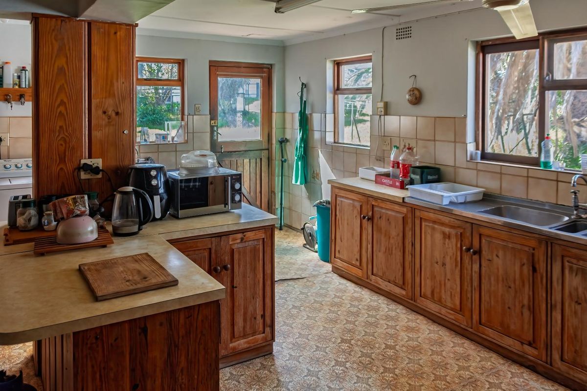A functional farm-style kitchen featuring wooden cabinetry, laminate countertops, a stainless steel sink, and multiple windows providing natural light.