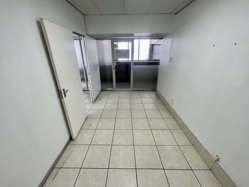 A vacant office space featuring tiled flooring, suspended ceiling, and aluminium-framed glass partitioning, offering a clean and functional layout for commercial use.