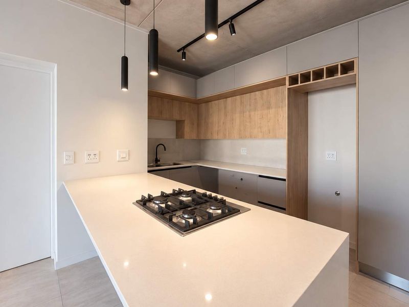 Modern kitchen featuring a central island with a gas hob, sleek cabinetry, stone countertops, and an exposed concrete ceiling with contemporary lighting.