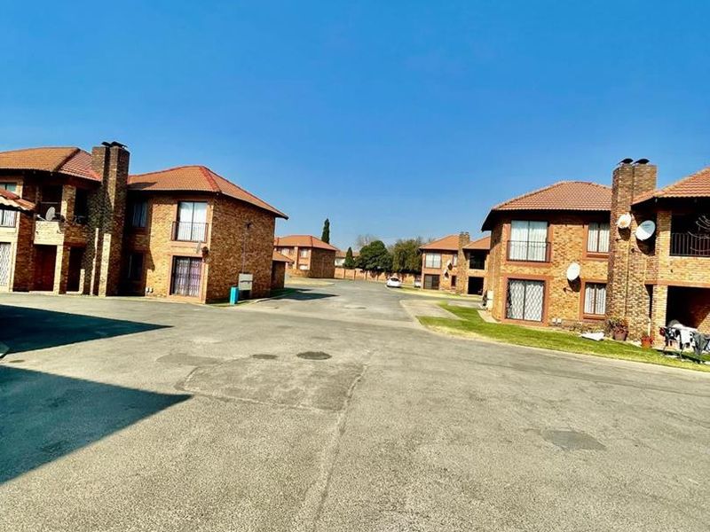 A view of the cluster complex featuring face-brick residential units with tiled roofs and a shared paved driveway.