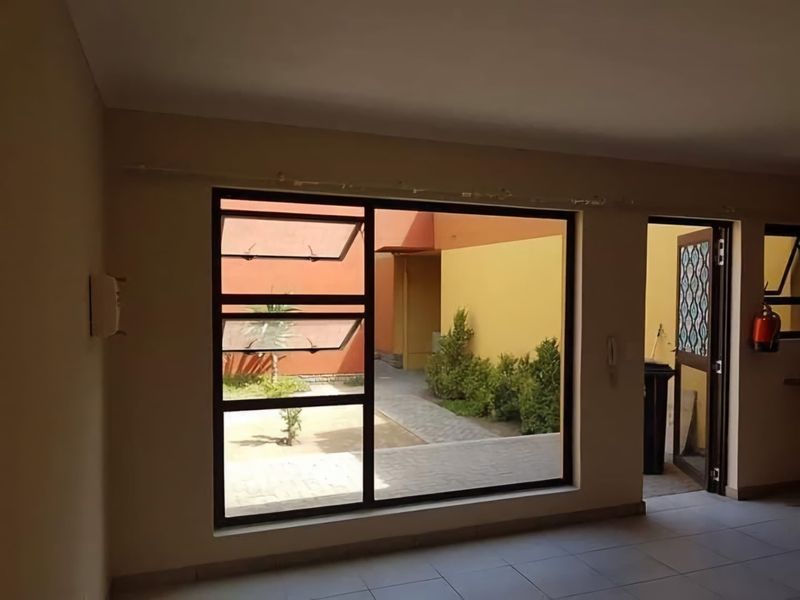 An empty living area featuring tiled flooring, a large aluminium window with top-hung sections, and direct access to an outdoor courtyard area.