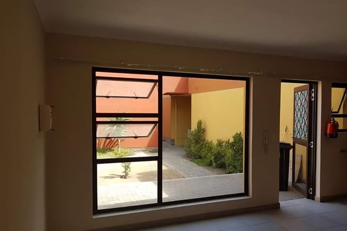 An empty living area featuring tiled flooring, a large aluminium window with top-hung sections, and direct access to an outdoor courtyard area.