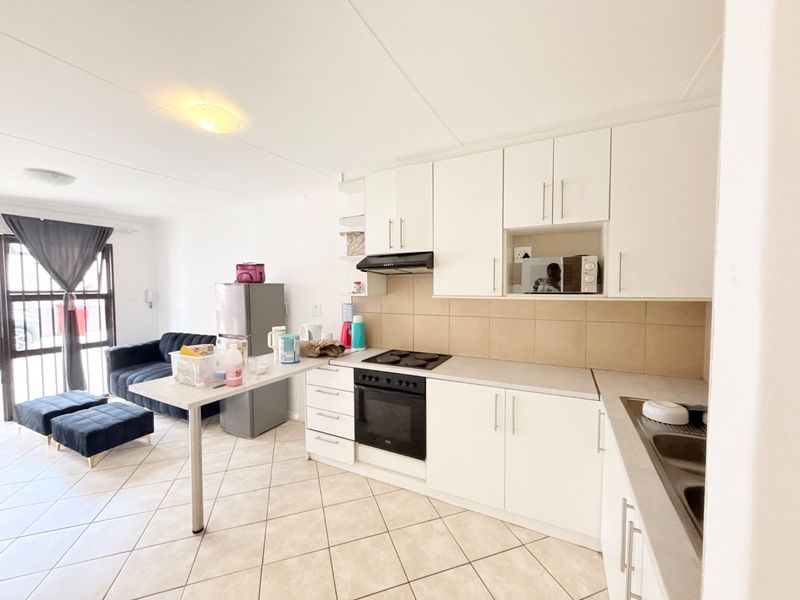 Open-plan kitchen and living area featuring white cabinetry, built-in oven and hob, tiled flooring, and a breakfast counter.