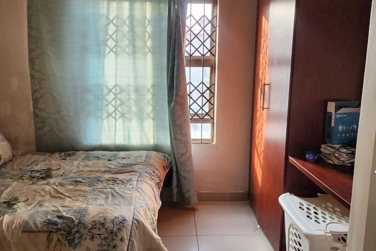 A bedroom featuring tiled flooring, a built-in wardrobe, and a window fitted with a security gate.