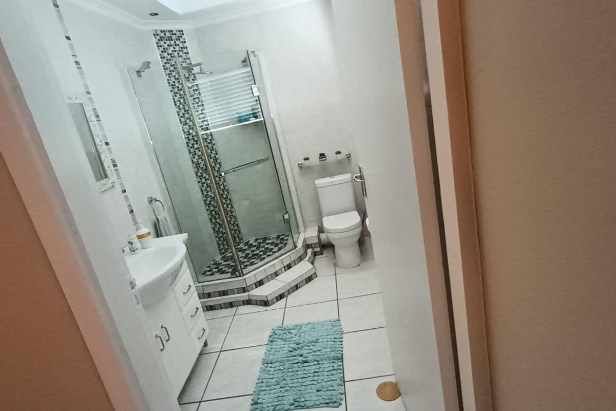 A functional bathroom featuring a corner shower enclosure, vanity cabinet with basin, and toilet, finished with neutral ceramic floor tiles.