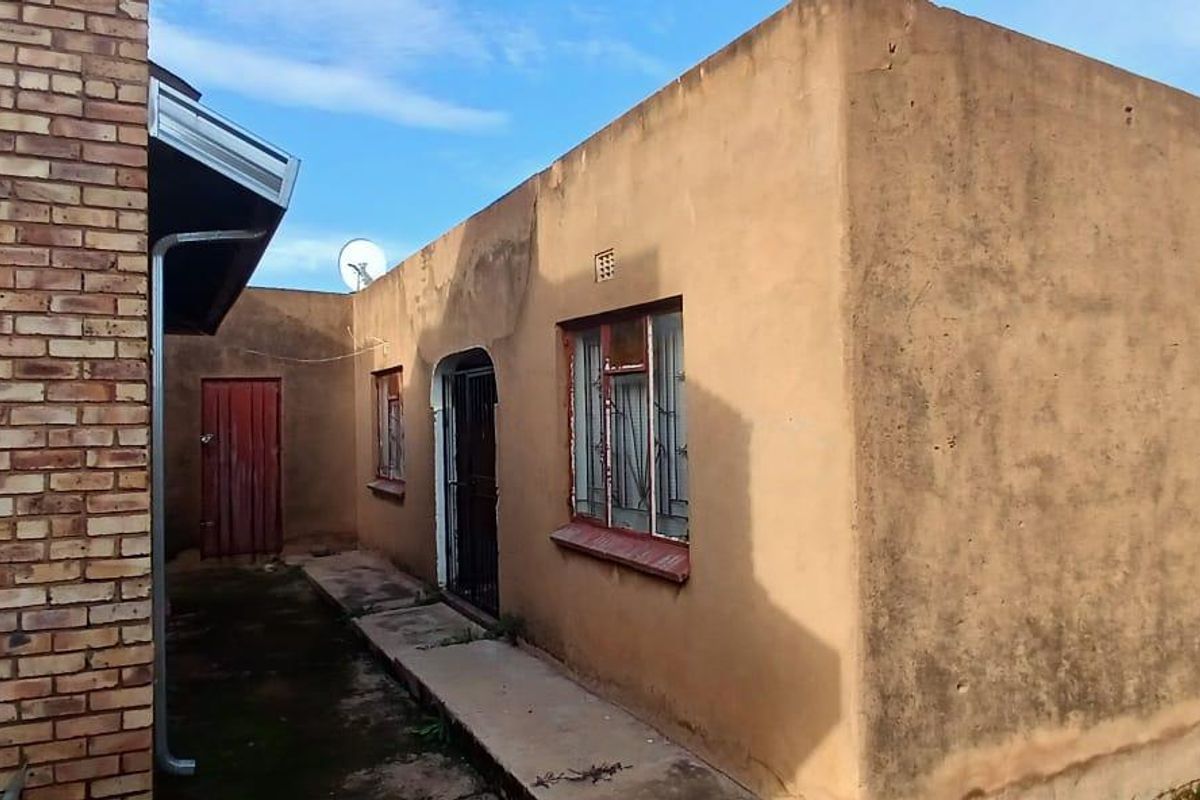 Rear exterior view of the property featuring a concrete walkway, brick and rendered walls, and metal security gates on windows and doors.