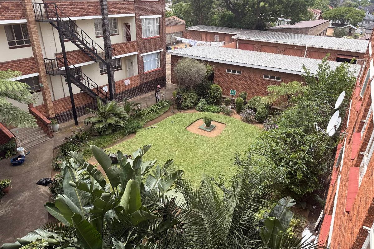 An elevated view of the apartment complex courtyard featuring a central lawn, landscaped garden beds, and communal brick buildings.